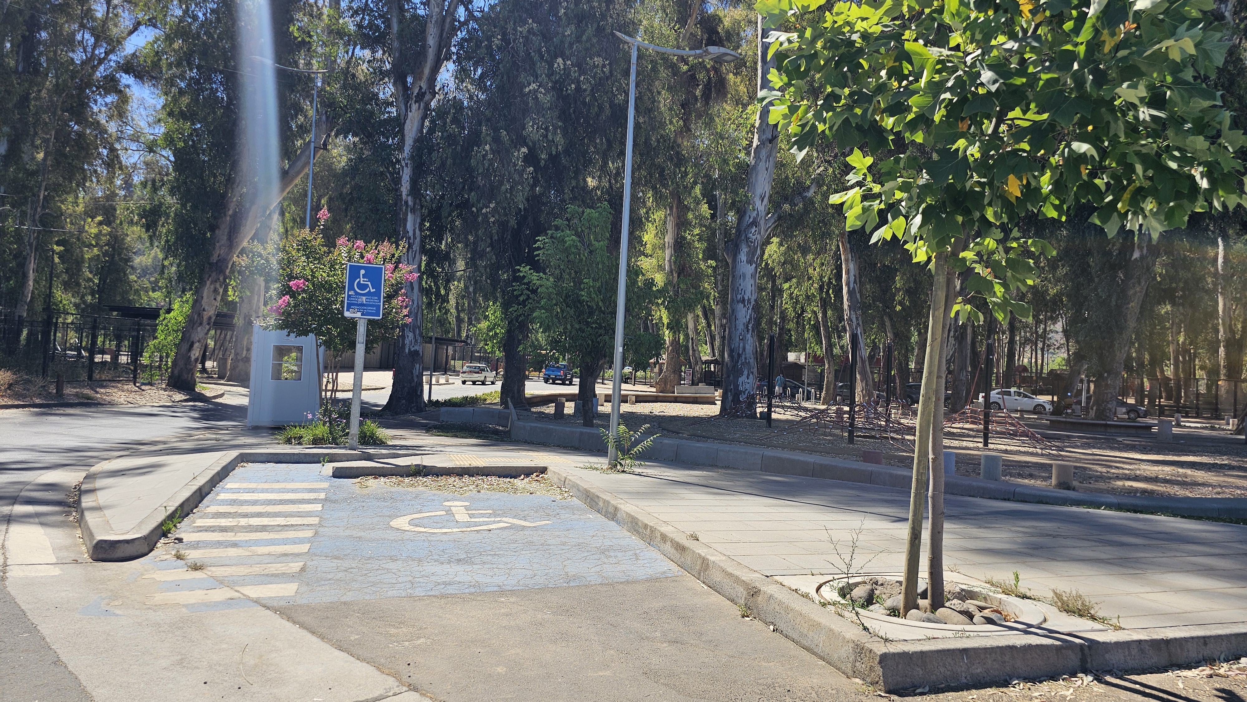Fotografía del Estacionamiento para personas con discapacidad, demarcado con el sector azul y letrero que destaca su reserva, también cuenta con el espacio para descender y una pequeña rampa para incorporarse al parque